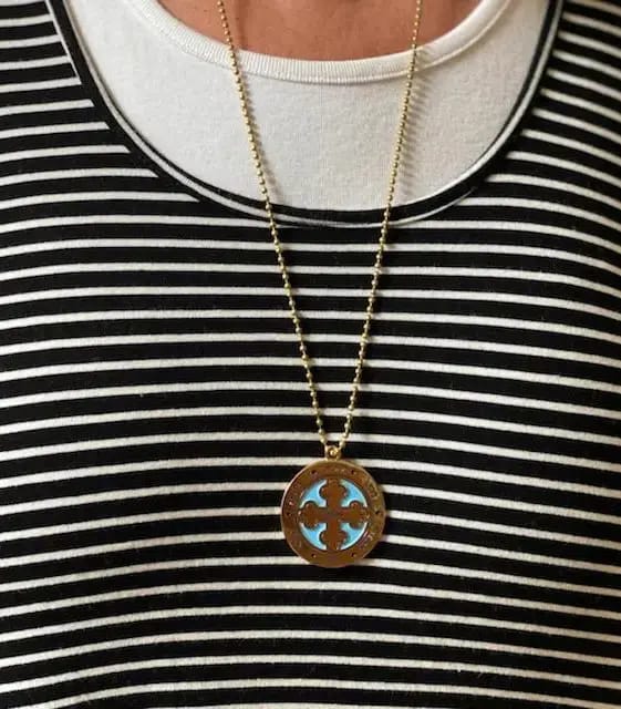 A person wearing a necklace with a wooden circle and blue arrows.