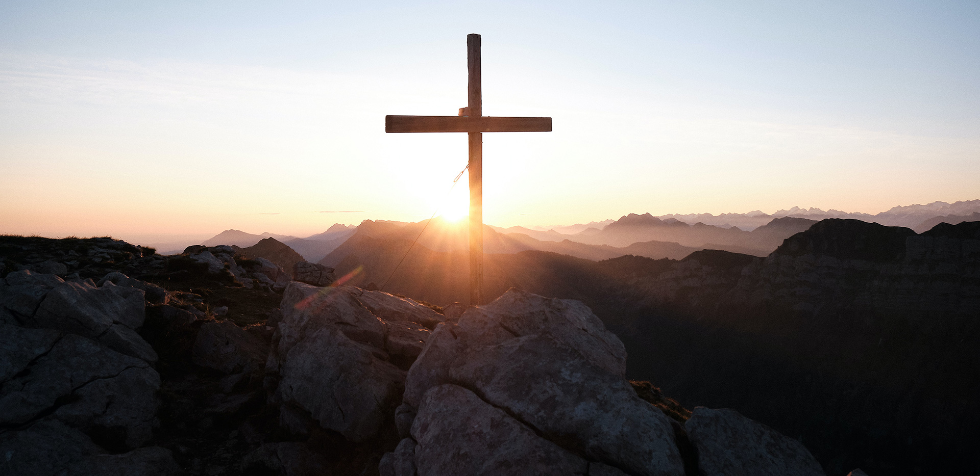A cross on top of a mountain with the sun setting.